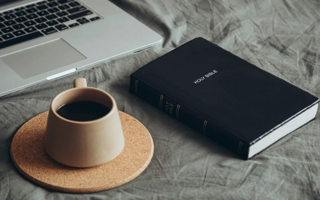 A coffee cup next to a book and computer Description automatically generated